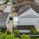 Luftaufnahme eines modernen Hauses mit Glasvordach und umgebenden GÀrten in einer stÀdtischen Nachbarschaft.