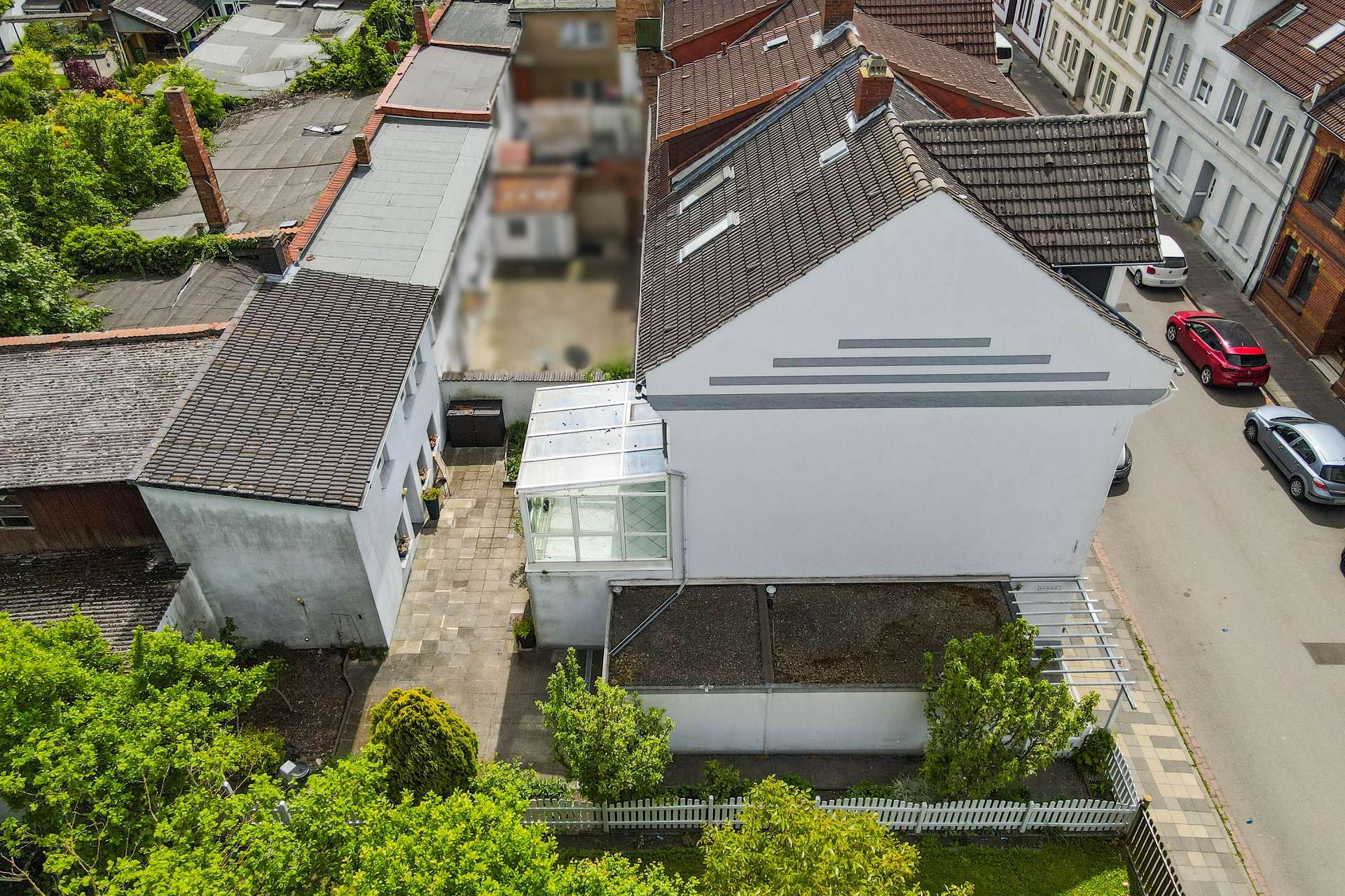 Luftaufnahme eines modernen Hauses mit Glasvordach und umgebenden GÀrten in einer stÀdtischen Nachbarschaft.