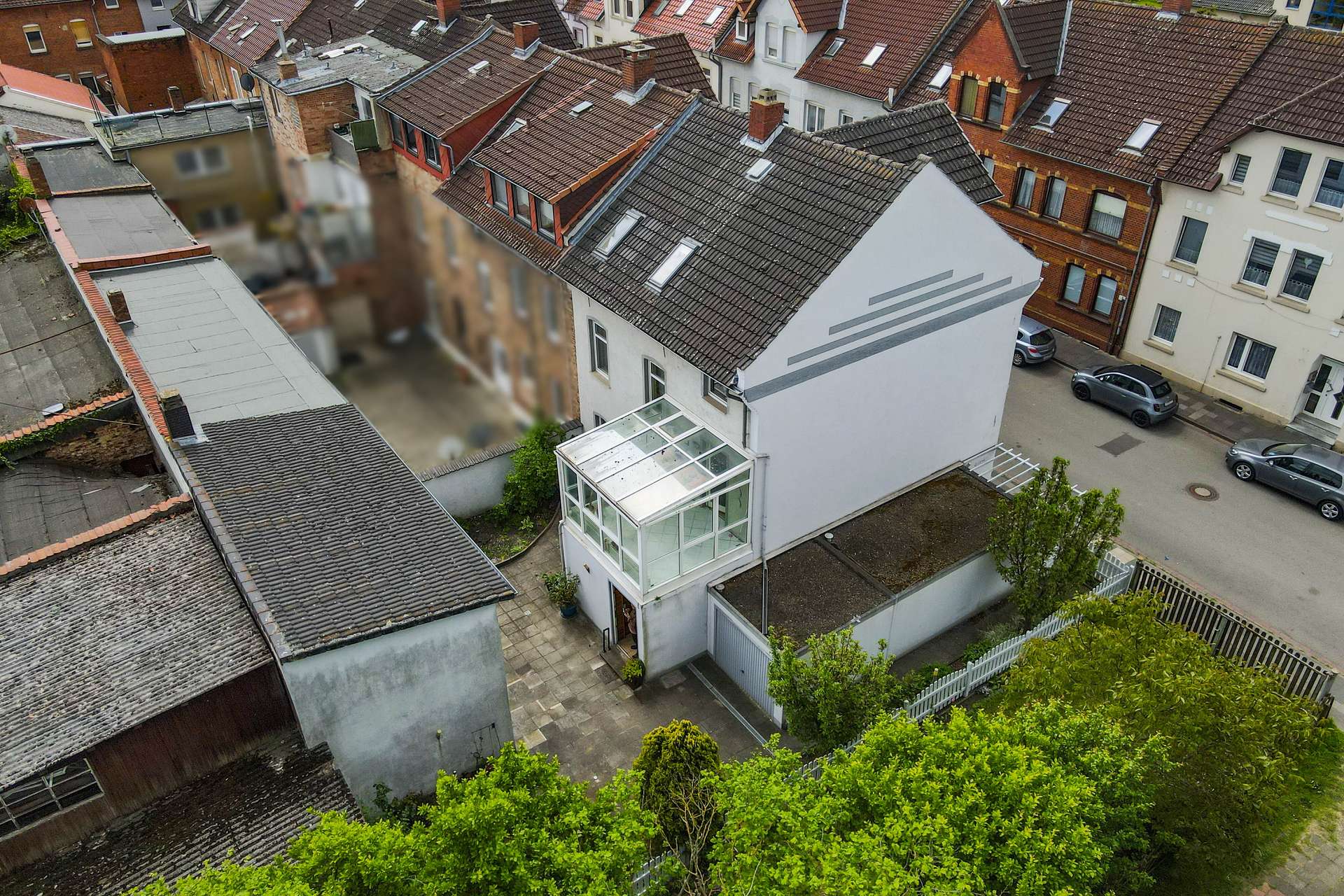 Luftaufnahme eines modernen Hauses mit Wintergarten, umgeben von traditionellen GebĂ€uden und grĂŒner Vegetation.