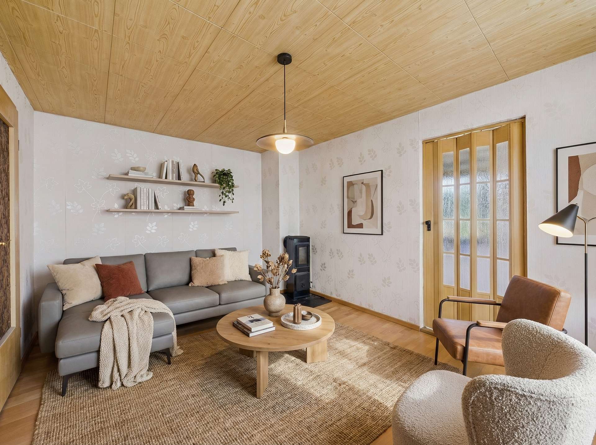 Helles Wohnzimmer mit grauem Sofa, runder Tisch, Teppich und moderner Beleuchtung, dekoriert mit Pflanzen und Kunstwerken.