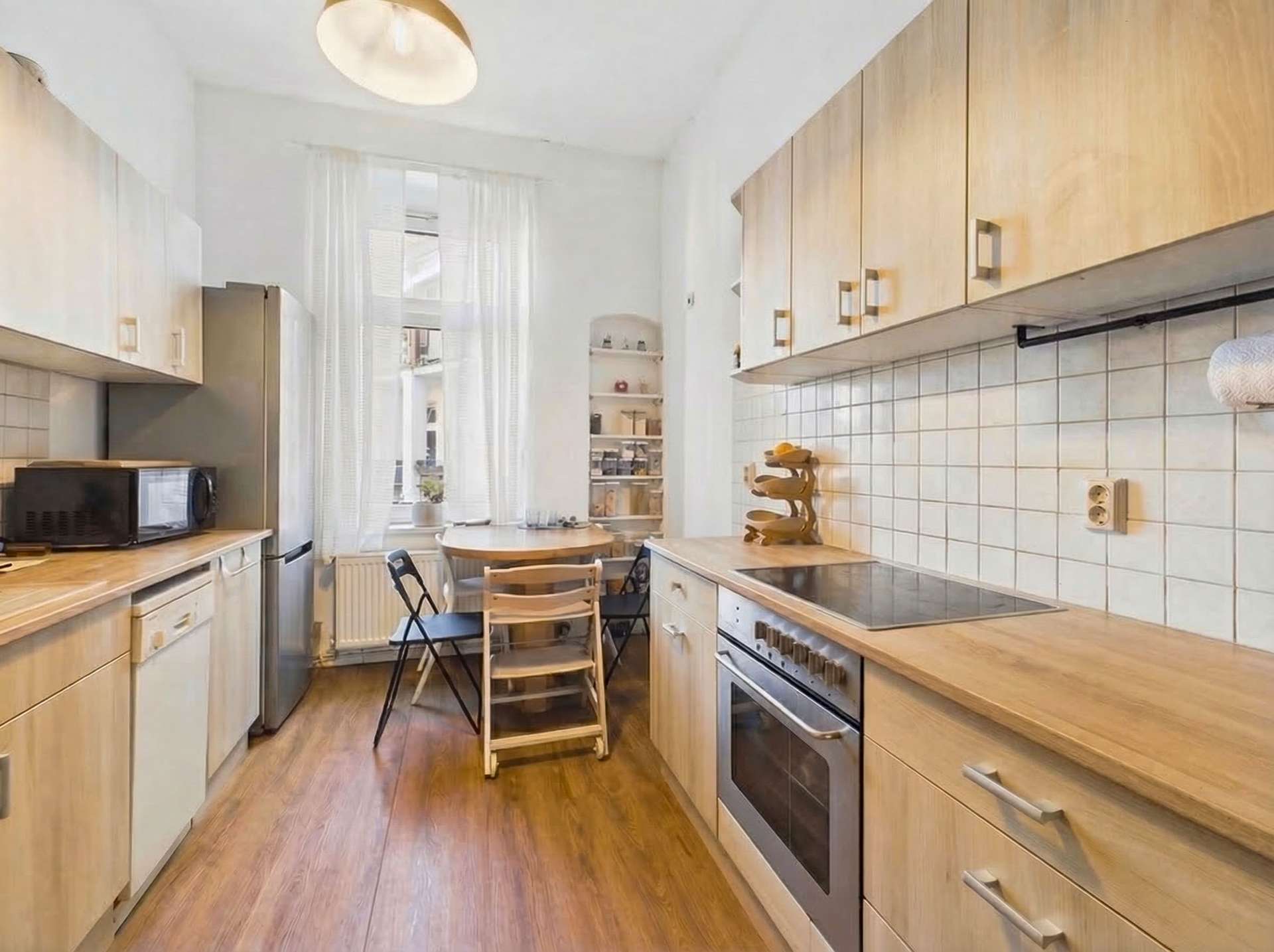 Moderne Küche mit Holzmöbeln, Elektrogeräten, Tisch mit Stühlen und Fenstern, die Tageslicht hereinlassen.