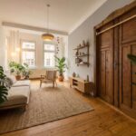 Helles Wohnzimmer mit Holzregal, Pflanzen, Couch und großen Fenstern, die eine gemütliche Atmosphäre schaffen.