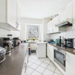 Moderne Küche mit hellen Schränken, Kühlschrank, Herd und Fenster, das Tageslicht hereinlässt.