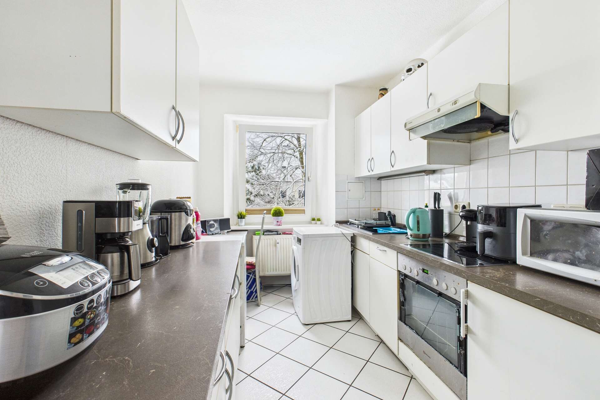 Moderne Küche mit hellen Schränken, Kühlschrank, Herd und Fenster, das Tageslicht hereinlässt.