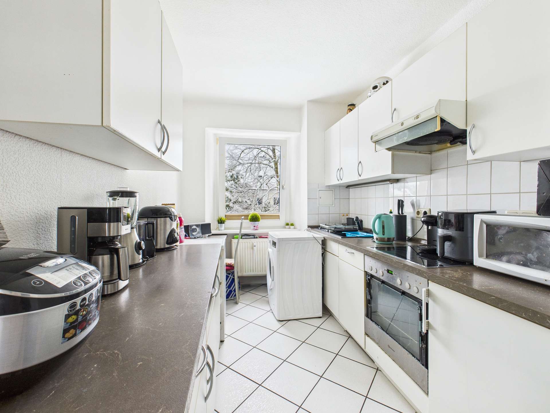 Moderne Küche mit hellen Schränken, Kühlschrank, Herd und Fenster, das Tageslicht hereinlässt.