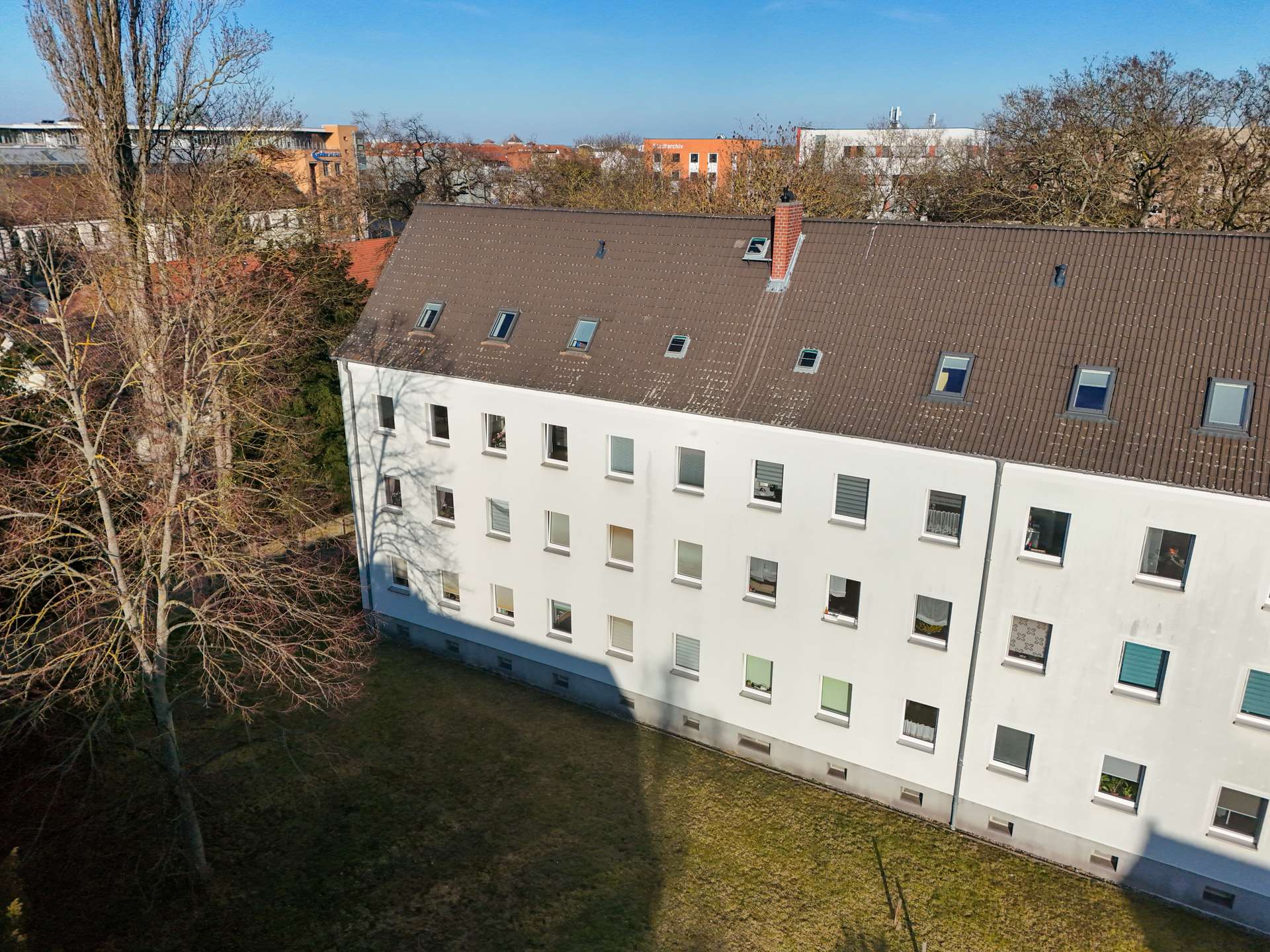 Ein mehrstöckiges, weißes Wohngebäude mit Fenstern und einem grünen Garten im Vordergrund, umgeben von Bäumen.
