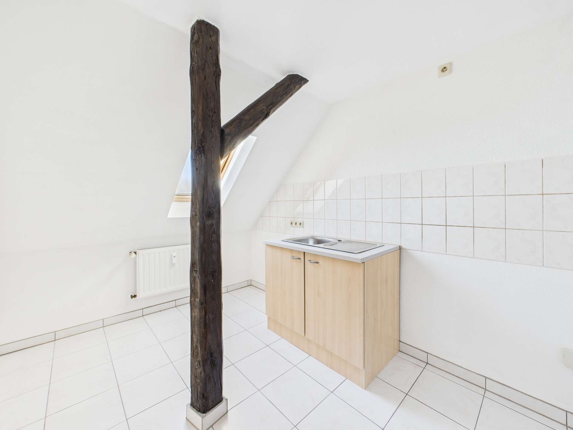 Küche mit Holzsäule und Dachschräge, ausgestattet mit Spüle und Fliesenboden.