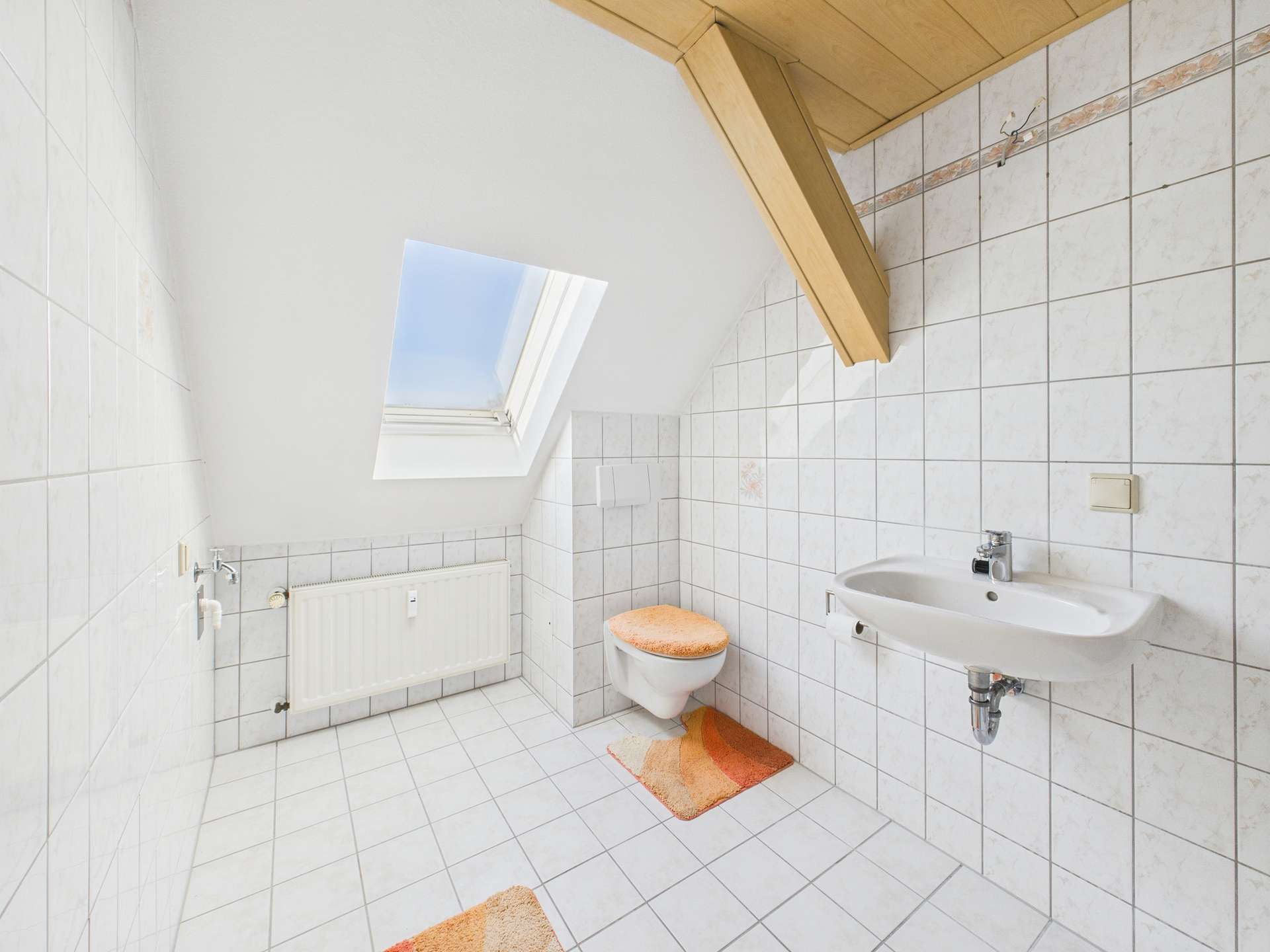 Helles Badezimmer mit Dachfenster, weißen Fliesen und Holzdecke, ausgestattet mit WC und Waschbecken.