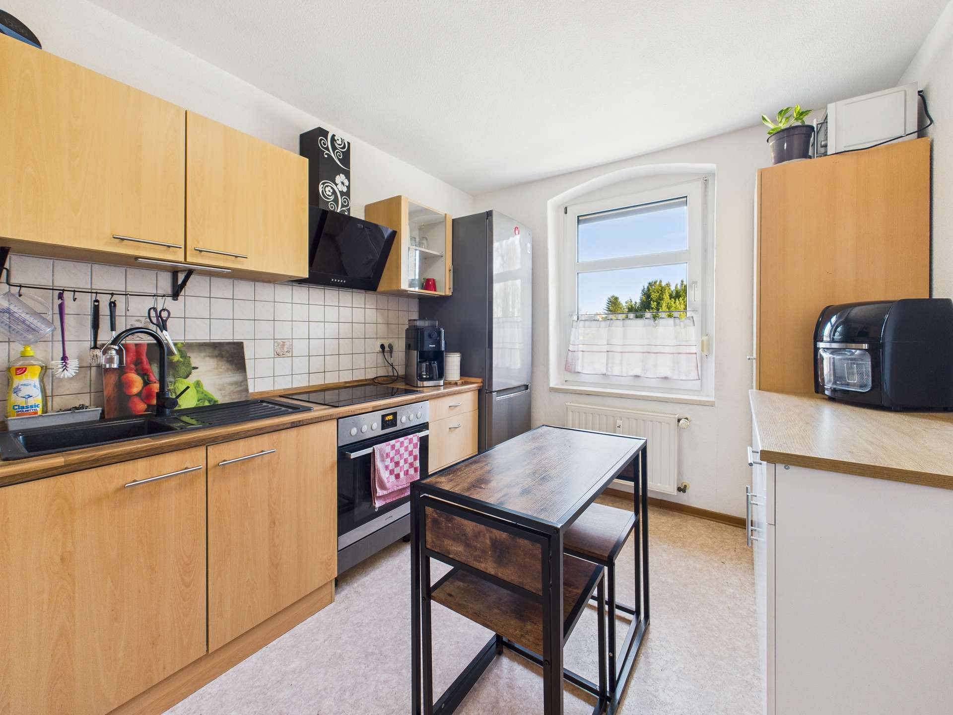 Helle moderne Küche mit Holzschränken, Herd, Kühlschrank und einem kleinen Tisch in der Mitte.