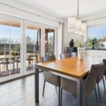 Heller Essbereich mit einem Holztisch, sechs Stühlen und großen Fenstern, die auf eine Terrasse blicken.