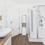 Modernes Badezimmer mit einer Dusche, Waschbecken und einem schmalen Schrank für Handtücher und Pflegeprodukte.