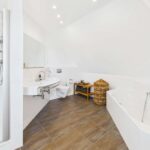 Modernes Badezimmer mit Dusche, Badewanne, Waschbecken und einem Korb aus geflochtenem Material. Helle, neutrale Farben.