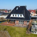 Ansicht eines modernen Hauses mit Solarpanelen, Garten, Terrasse und Gewächshaus in einer ruhigen Wohngegend.