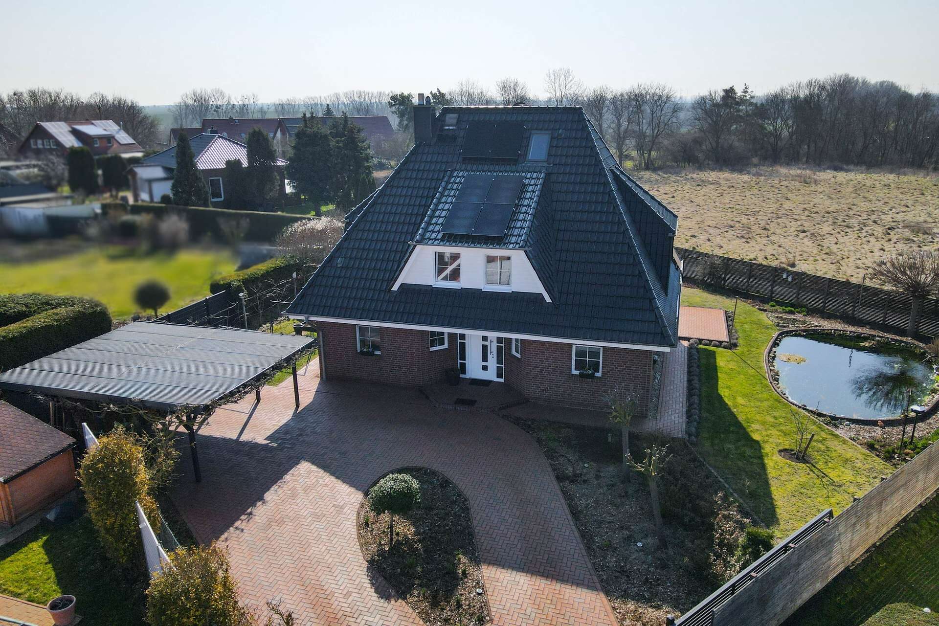 Ein modernes Einfamilienhaus mit Satteldach, umgeben von Rasenflächen und einem kleinen Teich.