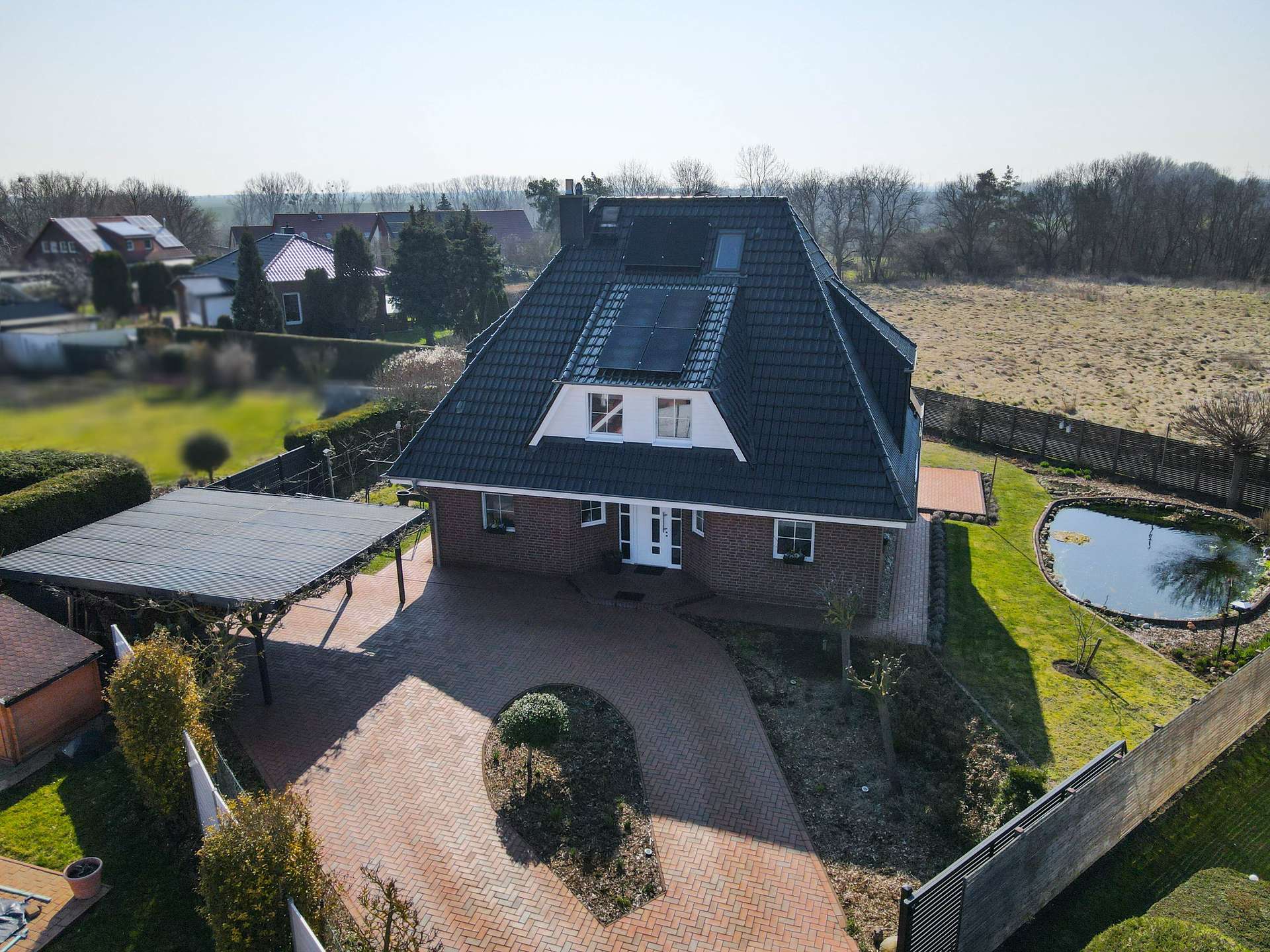 Ein modernes Einfamilienhaus mit Satteldach, umgeben von Rasenflächen und einem kleinen Teich.