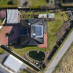 Dachansicht eines modernen Hauses mit Solarpanelen, Garten und Teich, umgeben von einem gepflegten Grundstück.