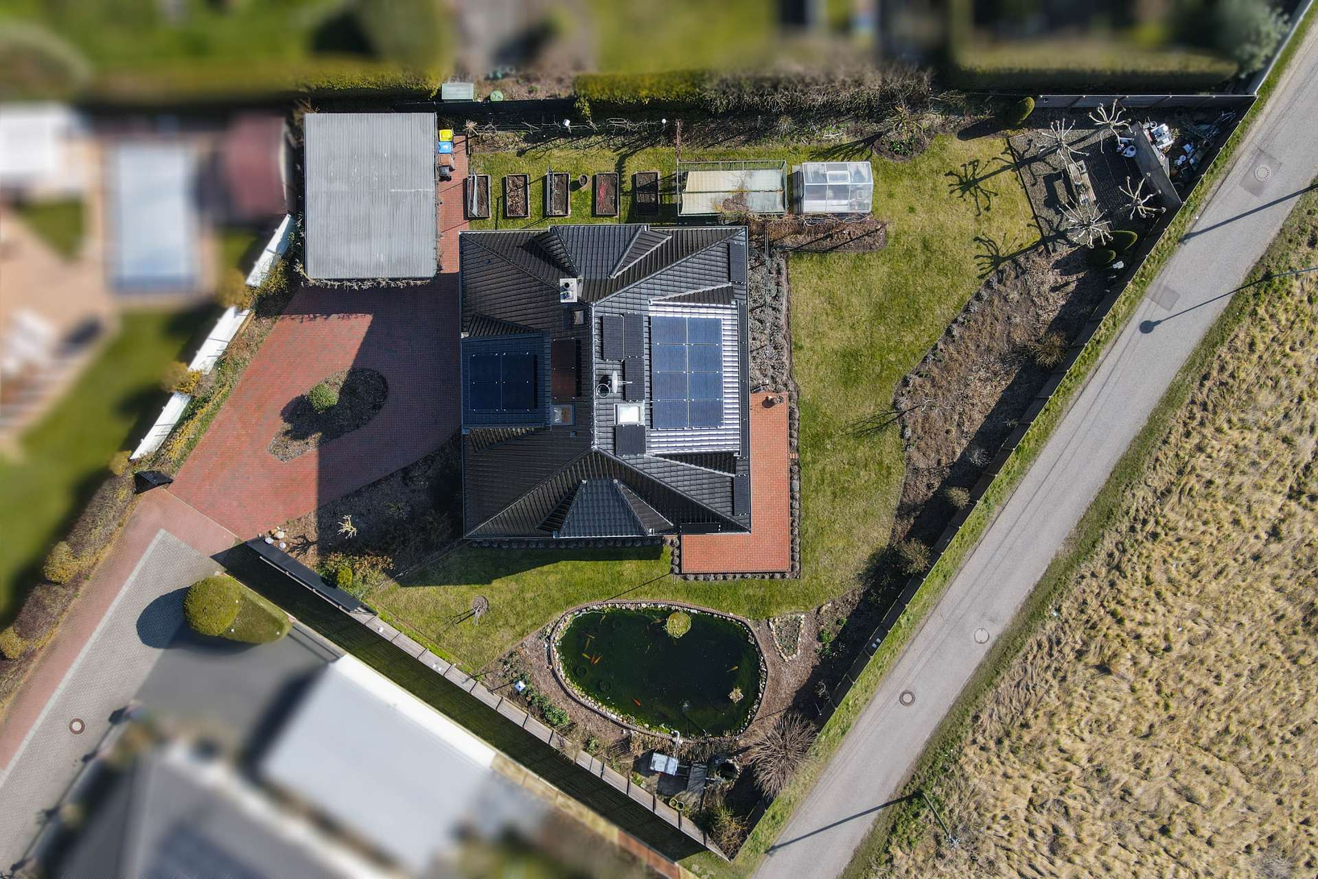 Dachansicht eines modernen Hauses mit Solarpanelen, Garten und Teich, umgeben von einem gepflegten Grundstück.