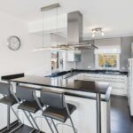 Moderne, helle Küche mit schwarzer Arbeitsplatte, Barhockern und großen Fenstern für viel Tageslicht.