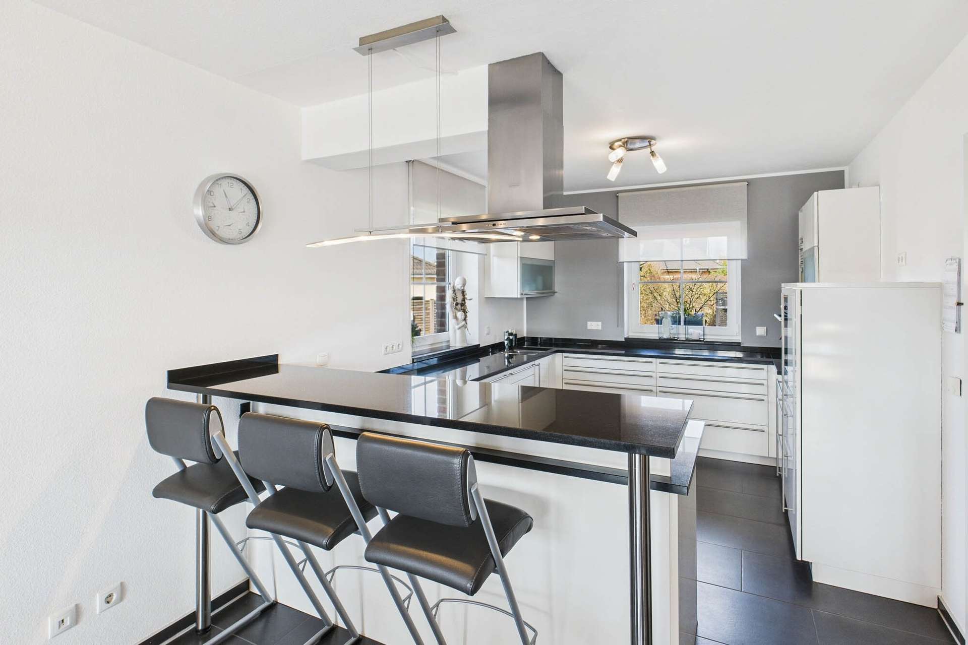 Moderne, helle Küche mit schwarzer Arbeitsplatte, Barhockern und großen Fenstern für viel Tageslicht.