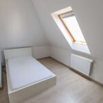 Helle Dachgeschosszimmer mit schrägen Wänden, einem Bett ohne Matratze und einem Fenster.