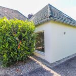 Ein modernes Haus mit einem großen, buschigen Strauch vor einem Fenster und gepflastertem Boden.