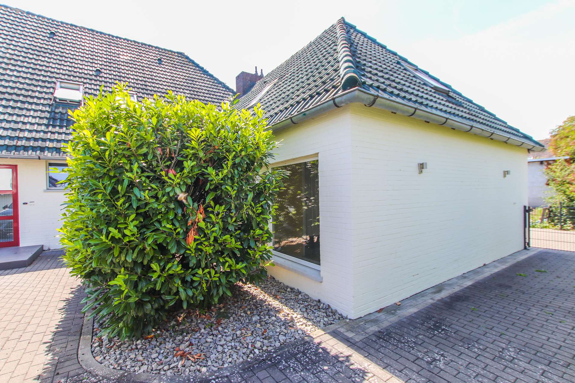 Ein modernes Haus mit einem großen, buschigen Strauch vor einem Fenster und gepflastertem Boden.