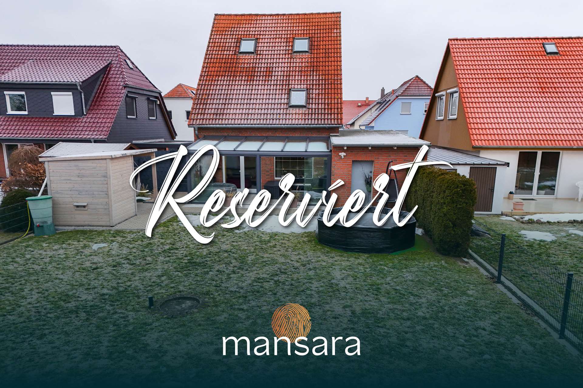 Hinteransicht eines Hauses mit Reservierungshinweis, umgeben von weiteren Wohngebäuden und einem gepflegten Garten.