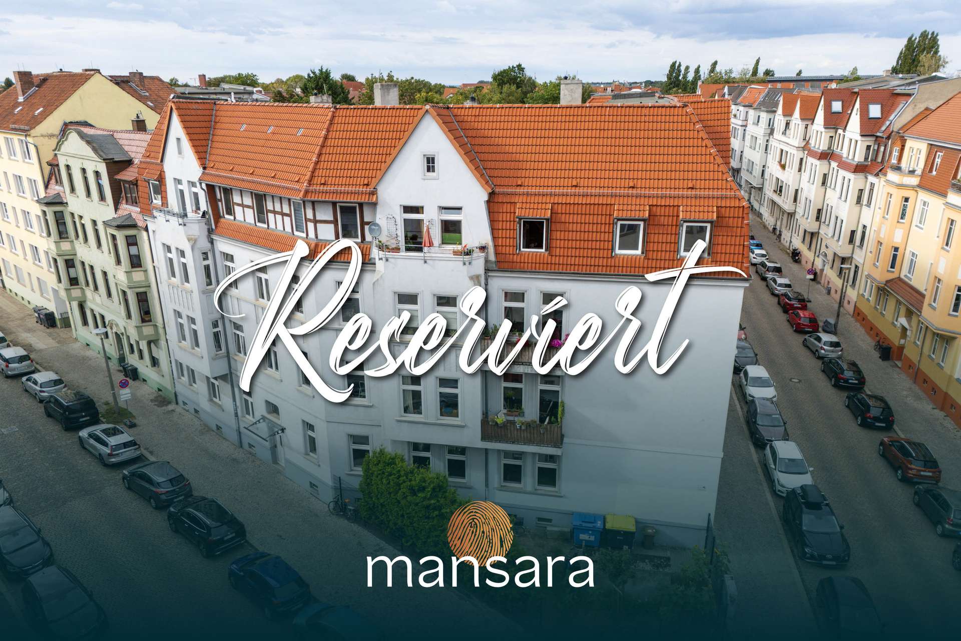 Ein mehrstöckiges Wohngebäude mit rotem Dach, umgeben von Straßen und parkenden Autos, mit dem Schriftzug „Reserviert“.