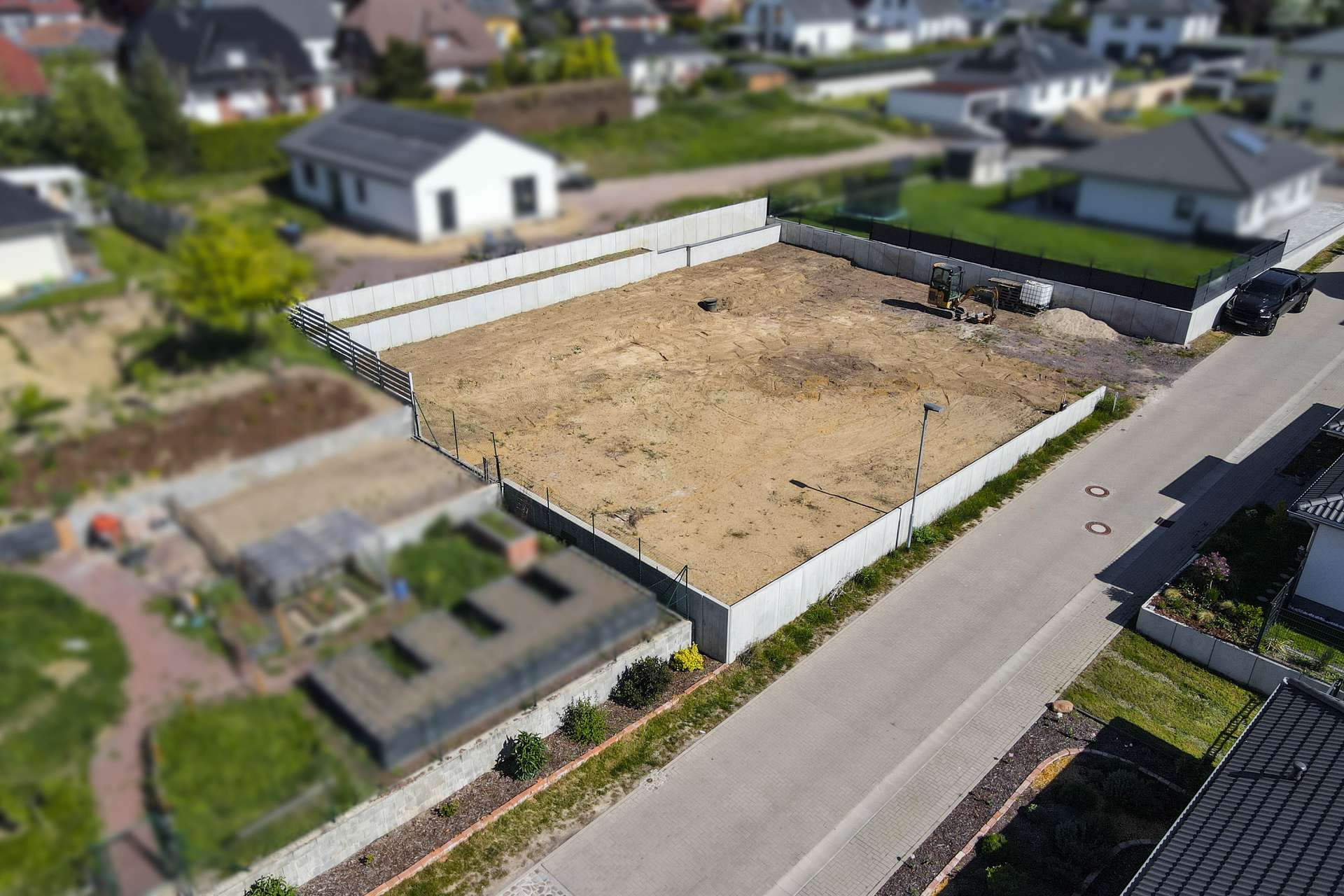 Unbebaute Grundstücksfläche umgeben von Zäunen, angrenzend an Wohngebäude und Gärten.