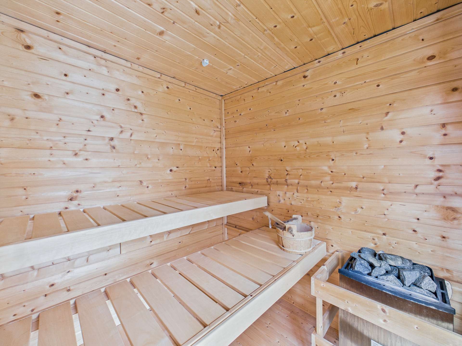 Holzverkleidete Sauna mit zwei Bänken, einem Eimer und Steinen für den Saunaofen.
