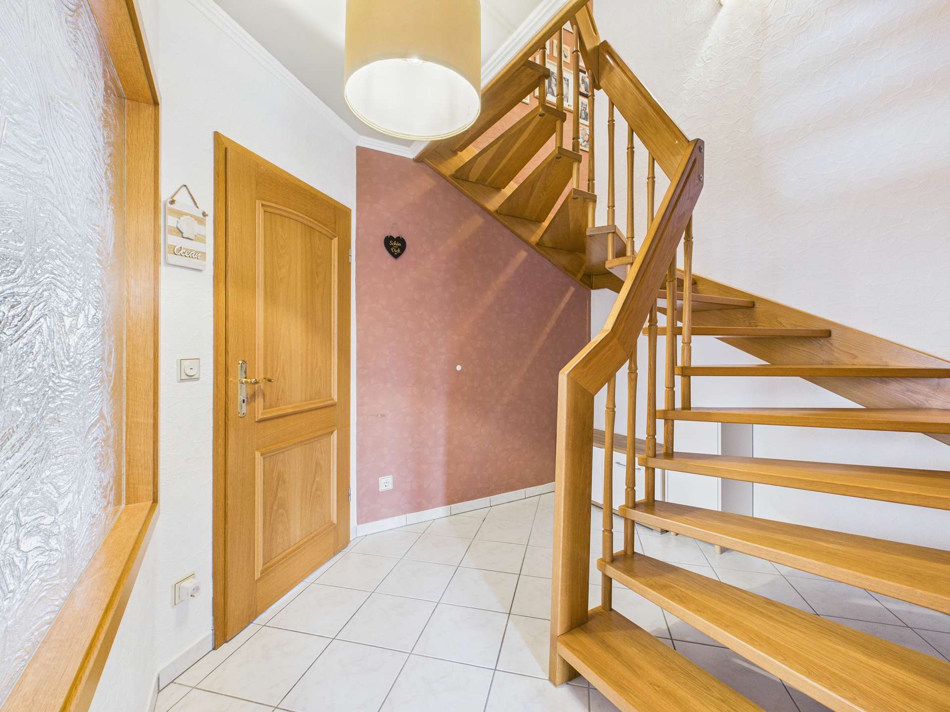 Helle Eingangshalle mit Holztreppe, weißer Wand und dekorativen Elementen.