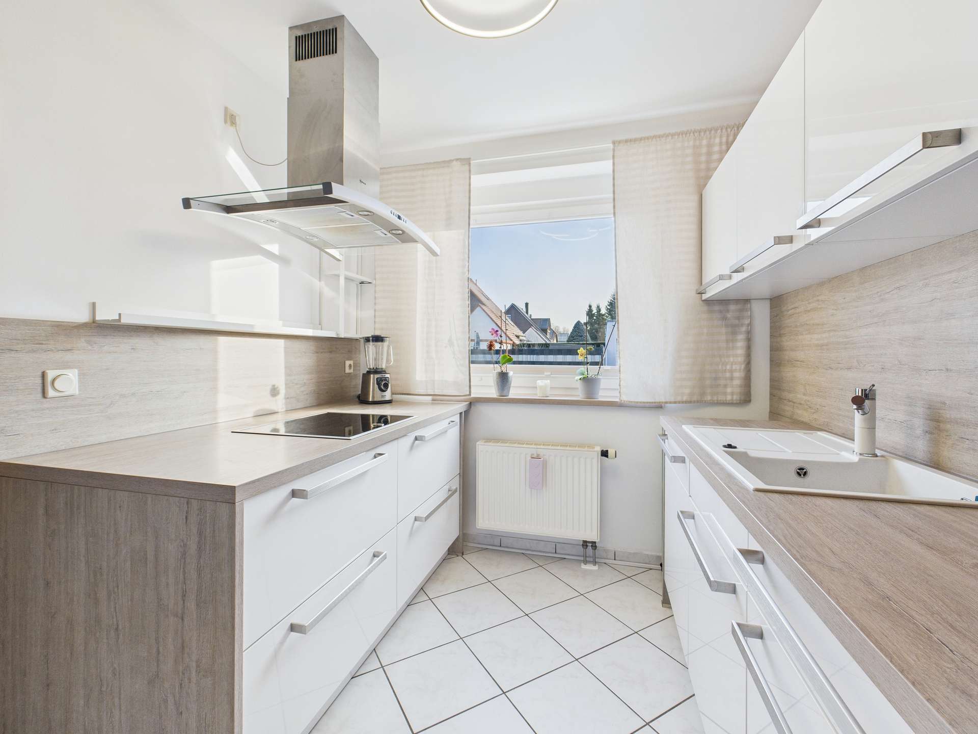 Moderne Küche mit weißen Schränken, Holzarbeitsflächen und Fensterblick auf die Außenlandschaft.