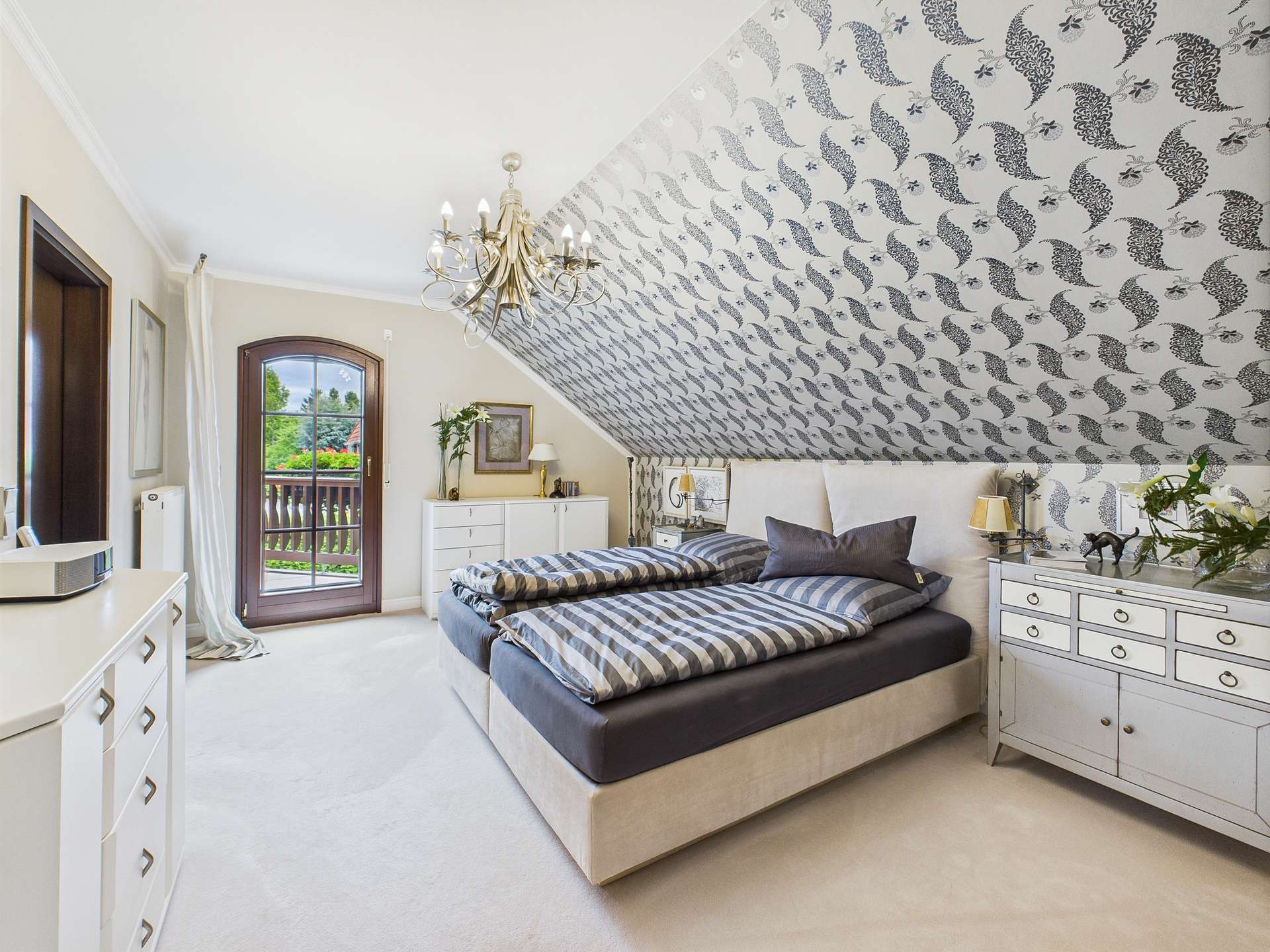 Schlafzimmer mit schrägem Dach, Doppelbett, eleganter Einrichtung und Fenster mit Blick auf die Natur.