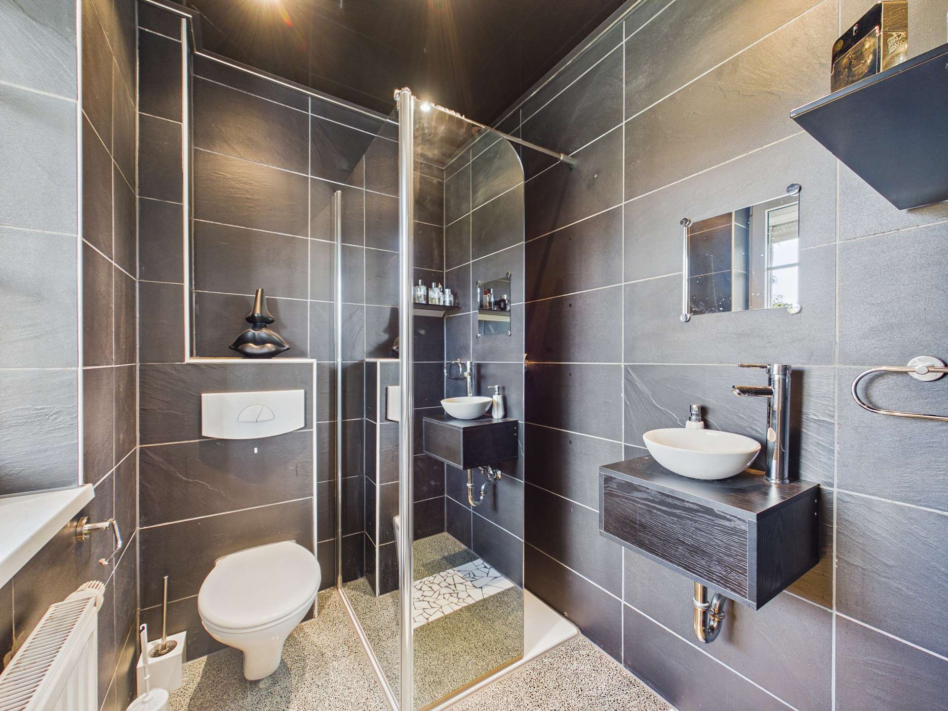 Modernes Badezimmer mit schwarzer Fliesenwand, Dusche, Waschbecken und WC. Minimalistisches Design und elegante Ausstattung.