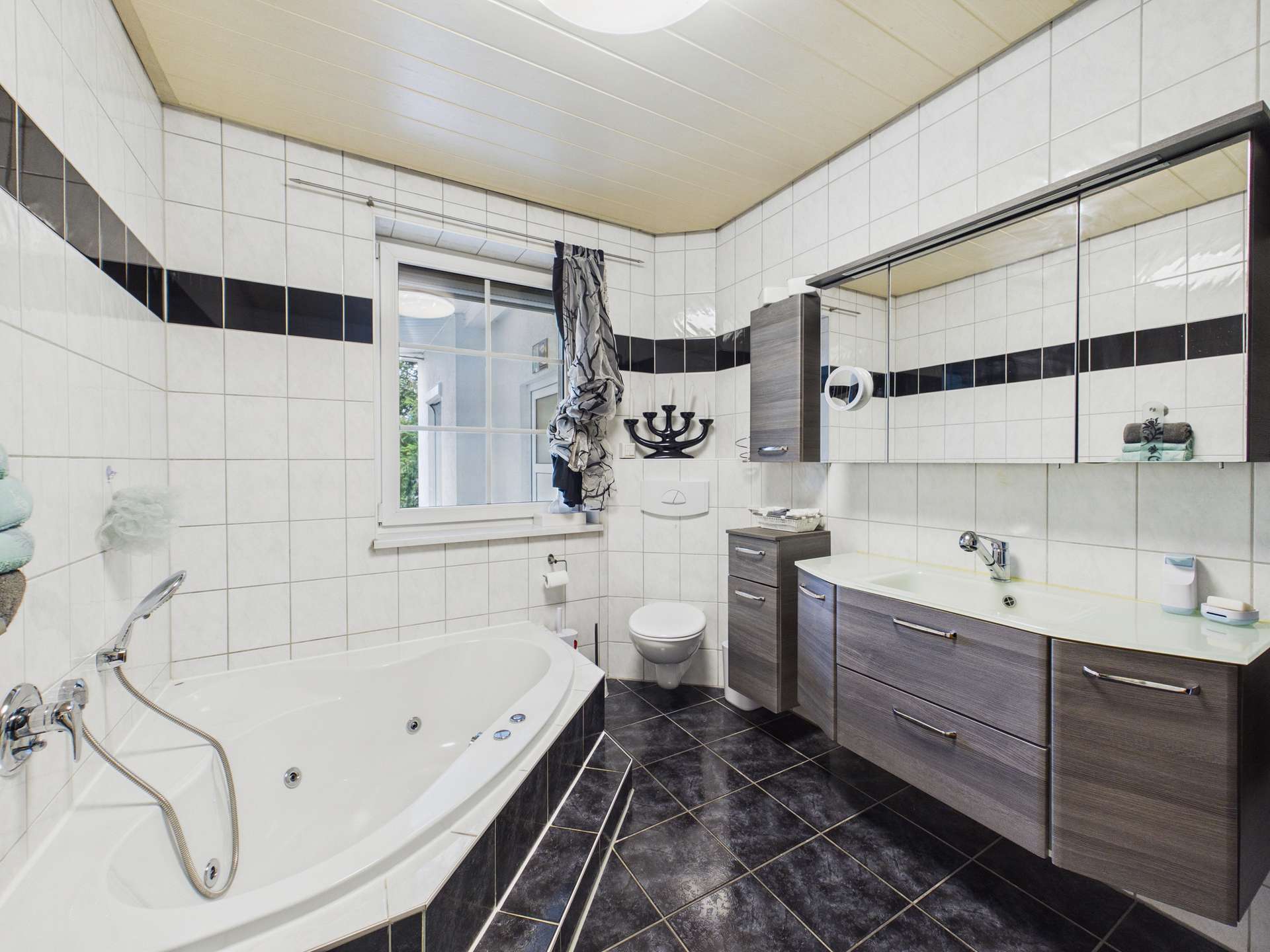 Modernes Badezimmer mit einer Badewanne, Dusche, WC und einem großen Spiegel. Weiße und schwarze Fliesen dominieren.