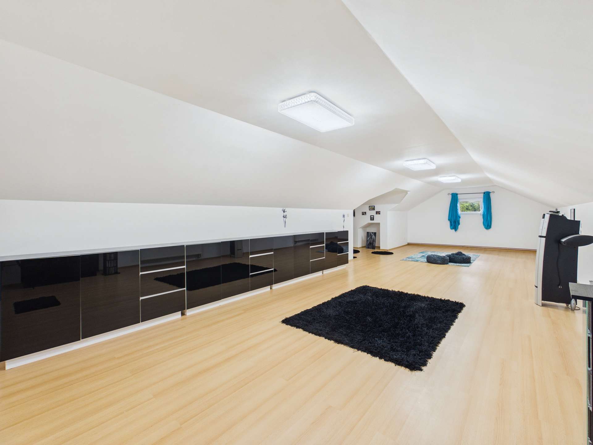 Geräumiger Dachboden mit hellen Wänden, dunklem Teppich, modernen Möbeln und großen Fenstern.