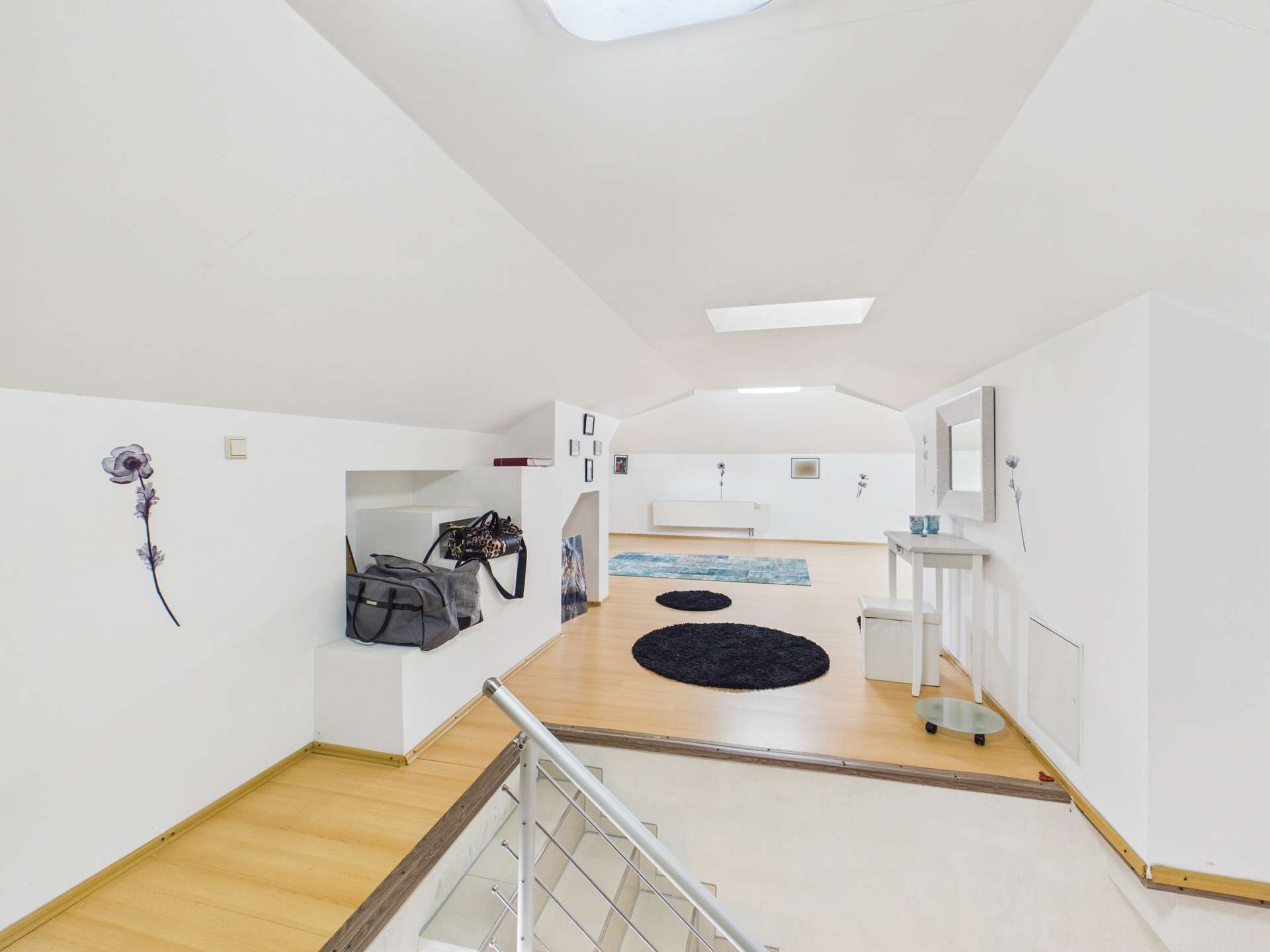 Helle, moderne Dachgeschosswohnung mit Holzfußboden, runder Teppich und minimalistischer Einrichtung.