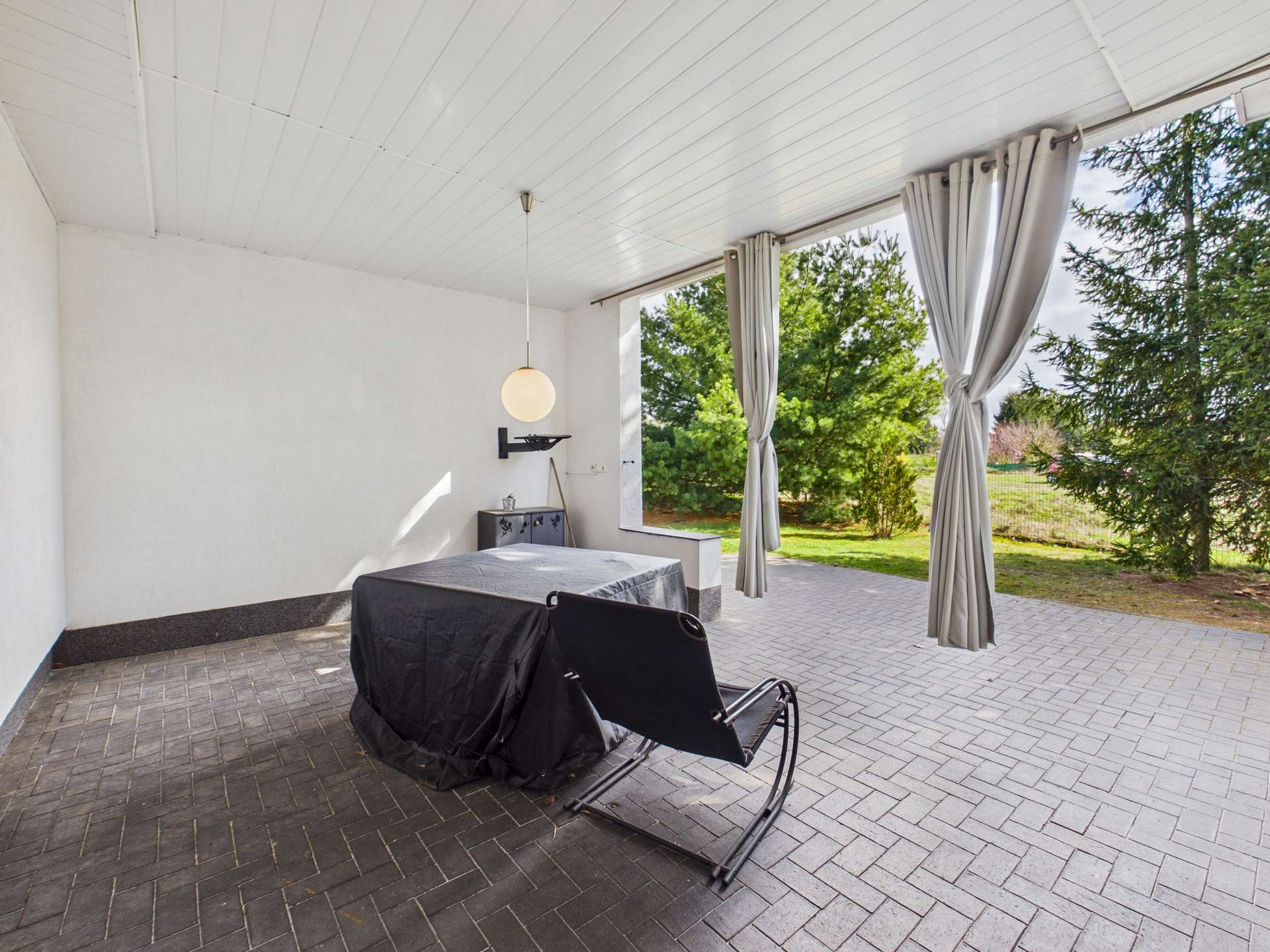 Ein moderner, heller Raum mit einem Tisch, einem Stuhl und großen Fenstern, die einen Blick auf den Garten bieten.