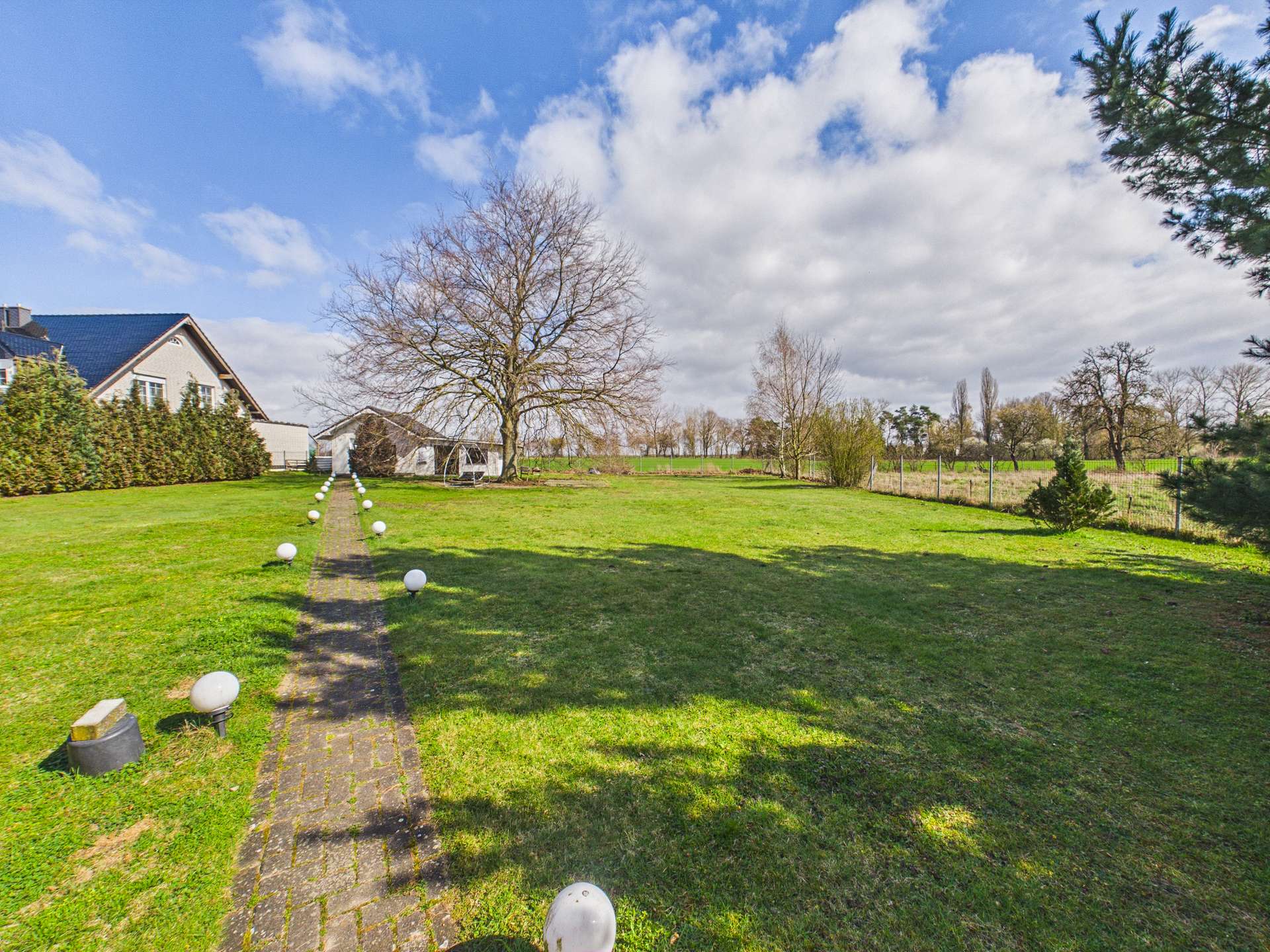 Weitläufiger Garten mit gepflastertem Weg, Bäumen und einem klaren Himmel im Hintergrund.