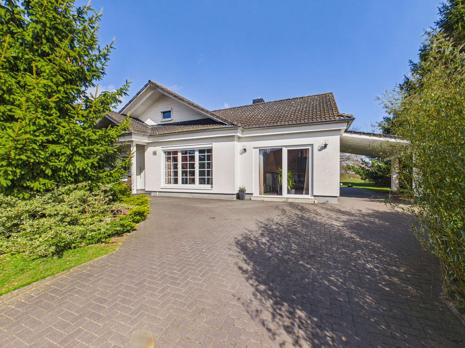 Ein modernes Einfamilienhaus mit großzügigem Eingang, großen Fenstern und angrenzendem Grünbereich.