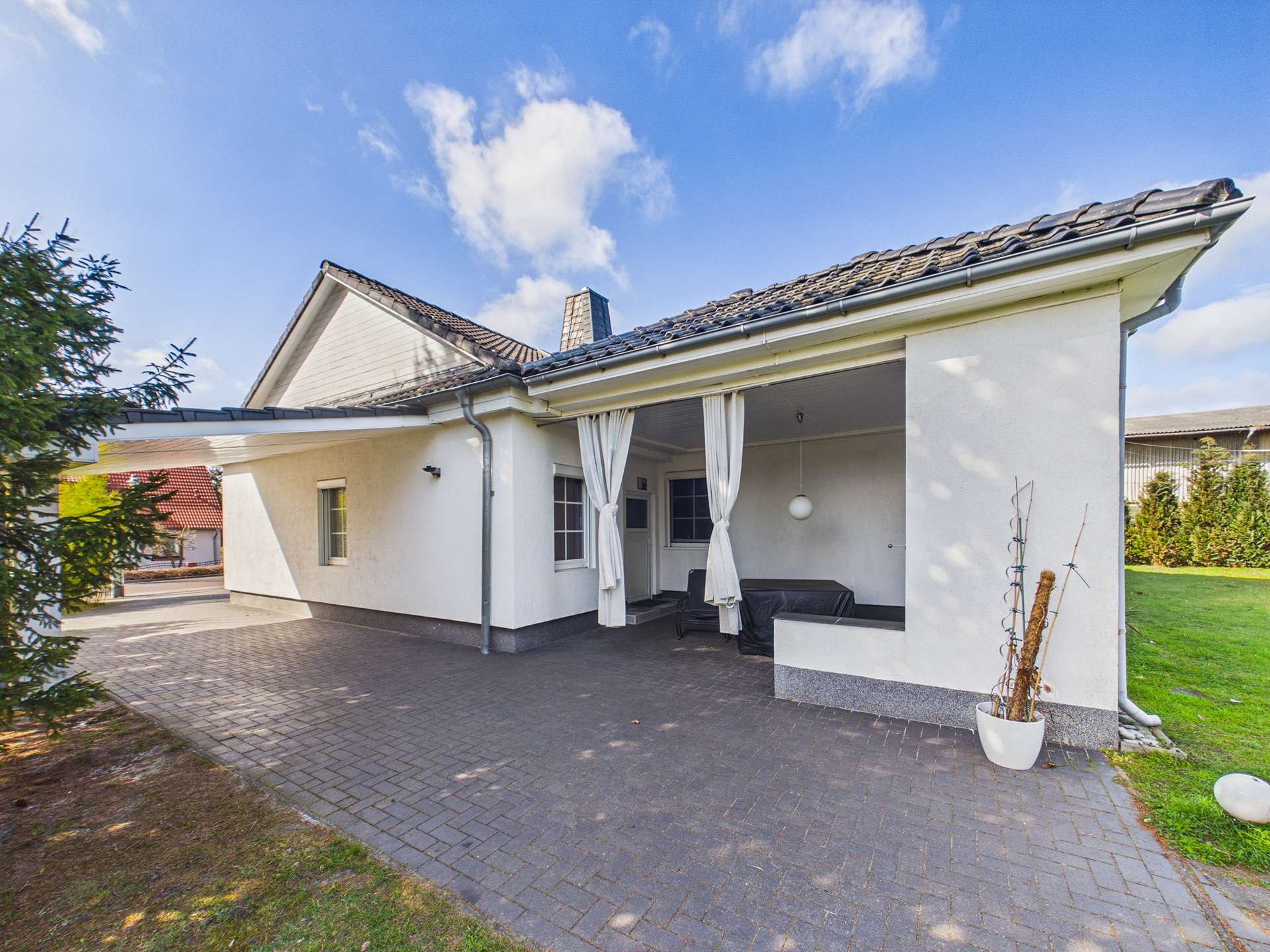 Modernes Einfamilienhaus mit überdachter Terrasse und Garten in sonniger Umgebung.