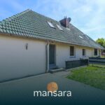 Ein modernes Einfamilienhaus mit grünem Dach und Terrasse, umgeben von Rasen und einem Parkplatz.