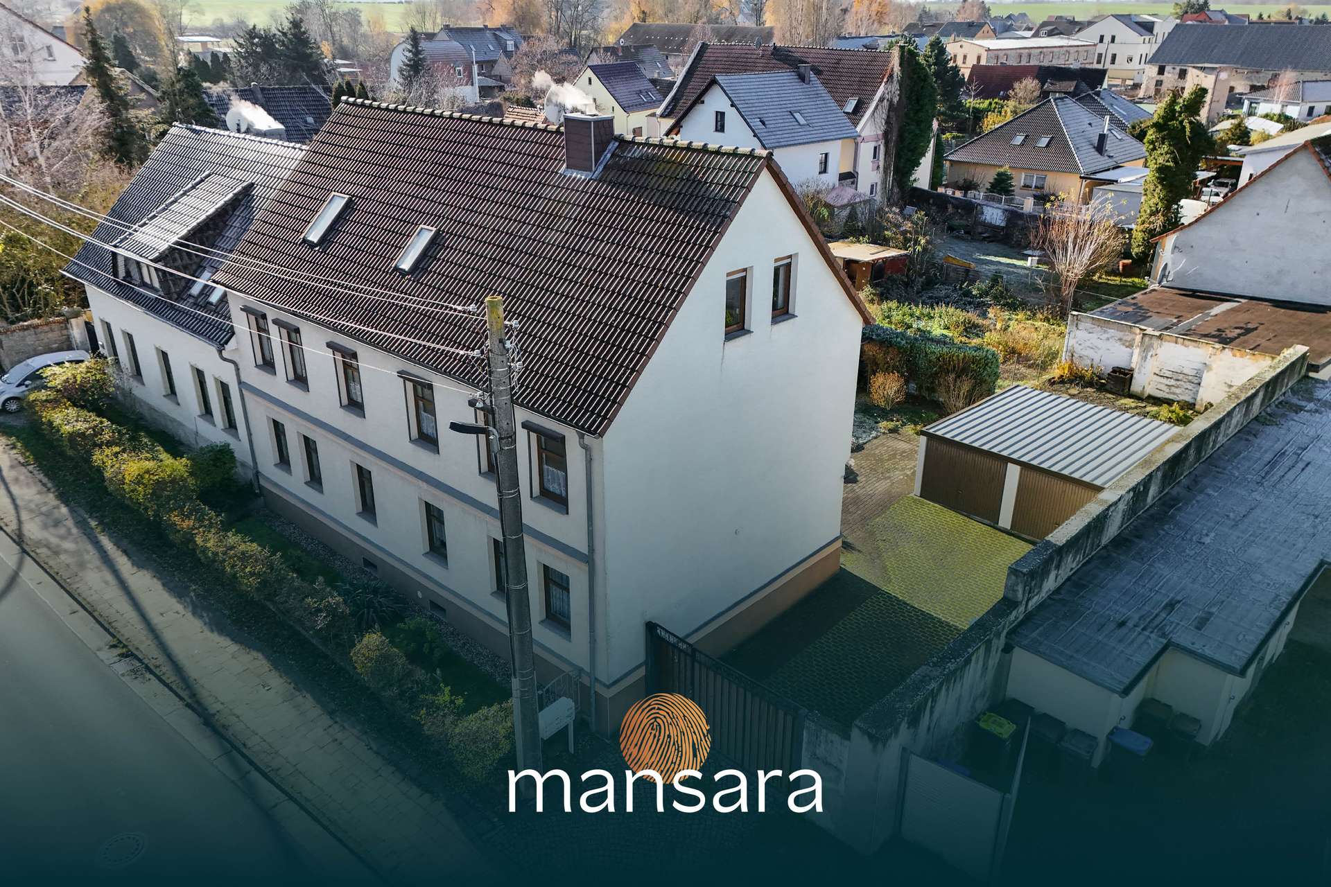 Zwei-stöckiges Wohngebäude mit Garten, umgeben von weiteren Häusern und Bäumen in einer ländlichen Umgebung.