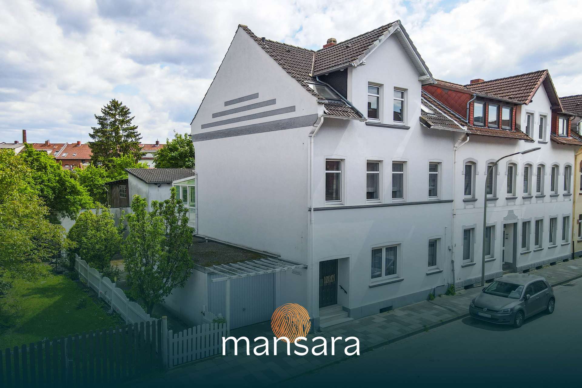Moderne Wohnhausfassade mit grauen Elementen, umgeben von Grünflächen und einem Parkplatz.