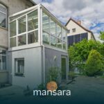 Glasveranda an einem Wohnhaus mit Garten und angrenzenden GebÀuden, unter einem bewölkten Himmel.