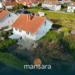 Zweifamilienhaus mit rotem Dach, umgeben von Grünflächen und Nachbarhäusern in einer ruhigen Wohngegend.