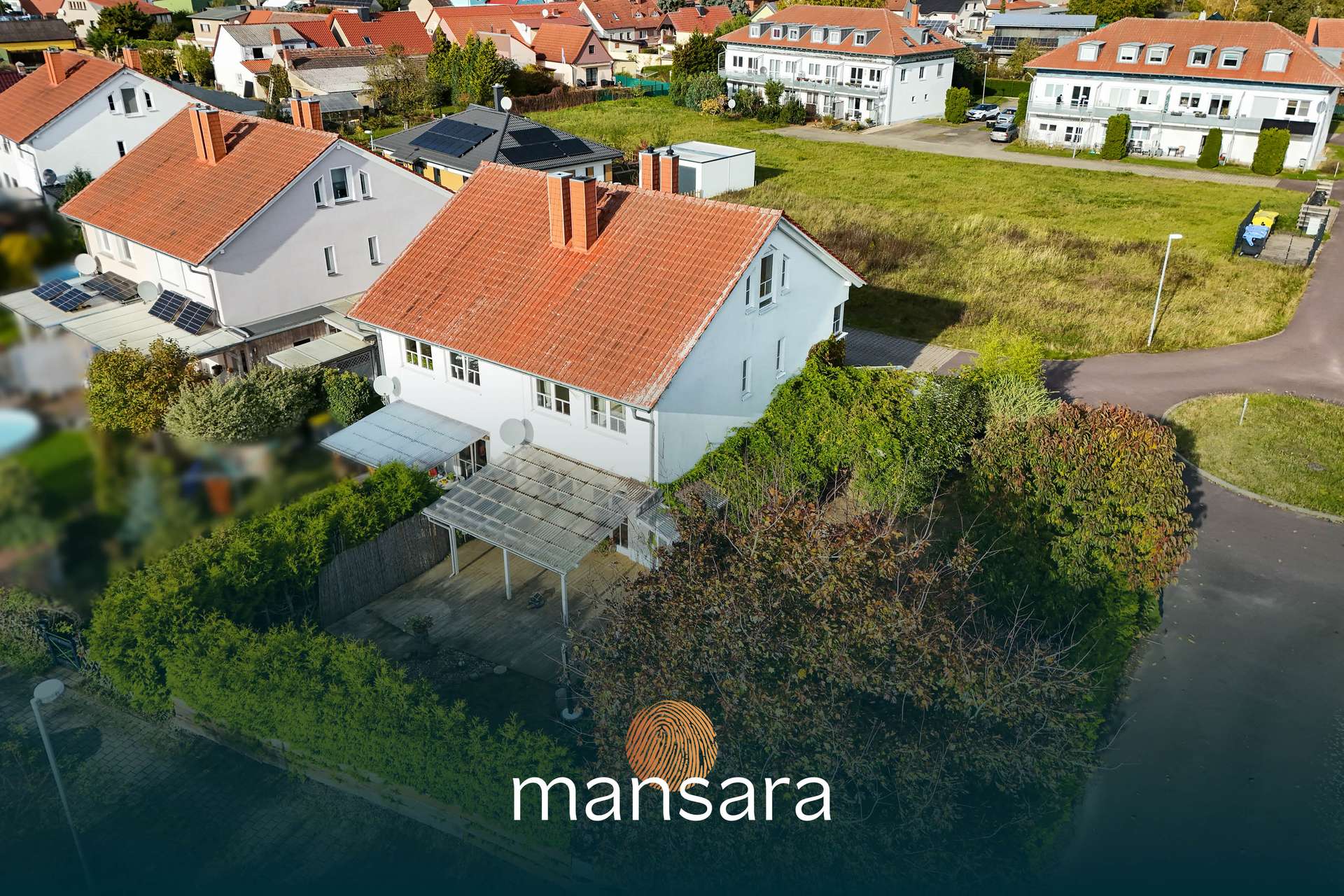 Zweifamilienhaus mit rotem Dach, umgeben von Grünflächen und Nachbarhäusern in einer ruhigen Wohngegend.