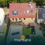 Luftaufnahme von Wohnhäusern mit einem Garten, umgeben von Bäumen und Fahrzeugen auf der Straße.