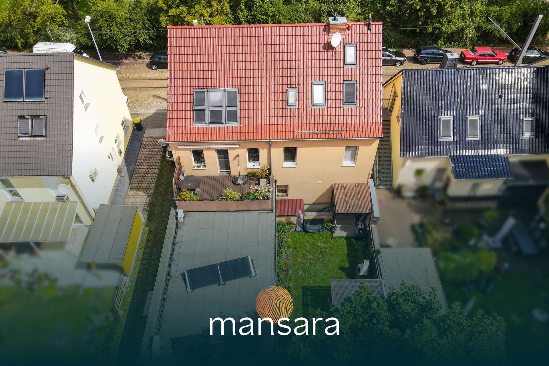 Luftaufnahme von Wohnhäusern mit einem Garten, umgeben von Bäumen und Fahrzeugen auf der Straße.