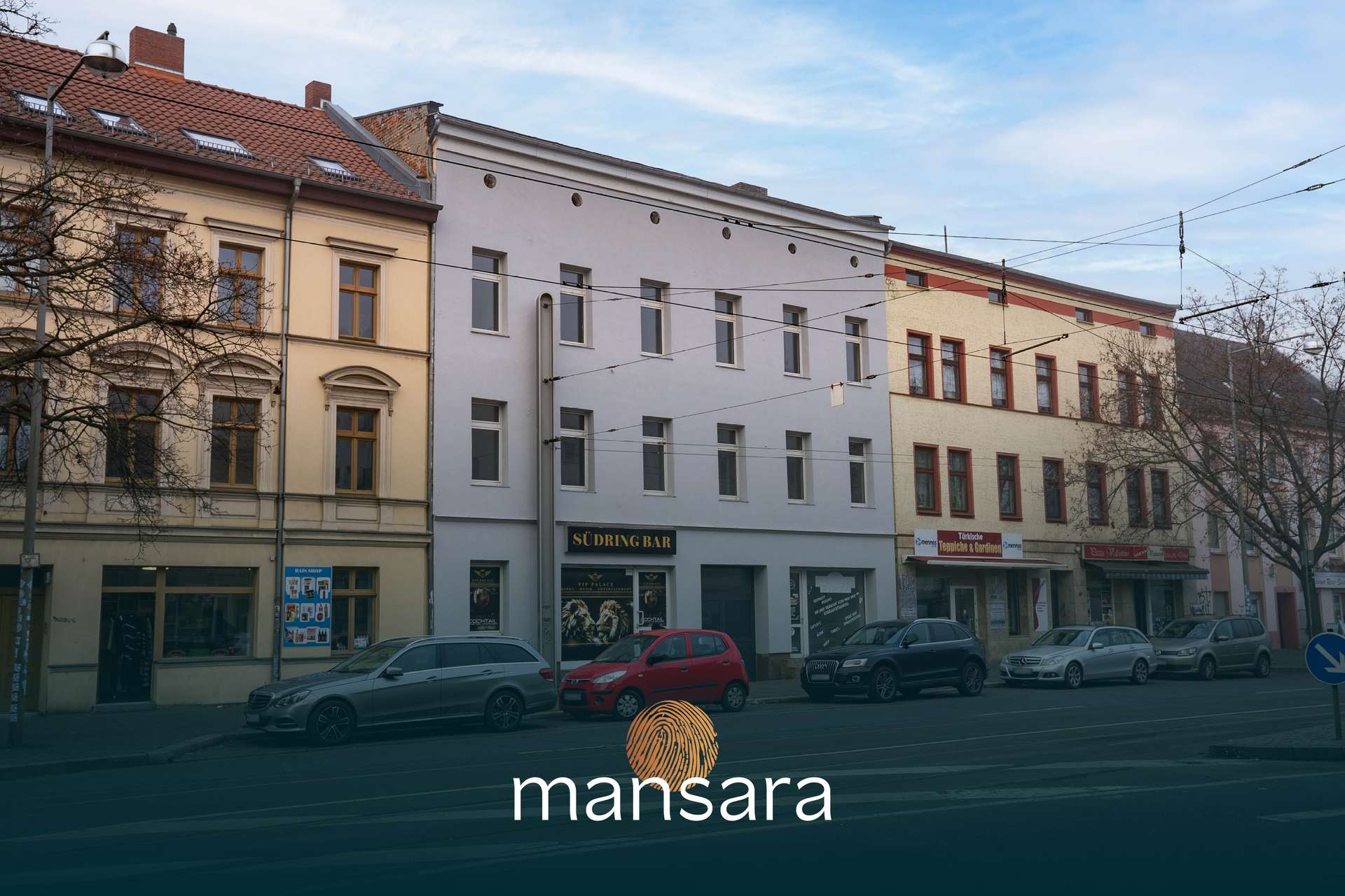 Stadtansicht mit mehreren Gebäuden, darunter ein Restaurant und geparkte Autos, bei bewölktem Himmel.